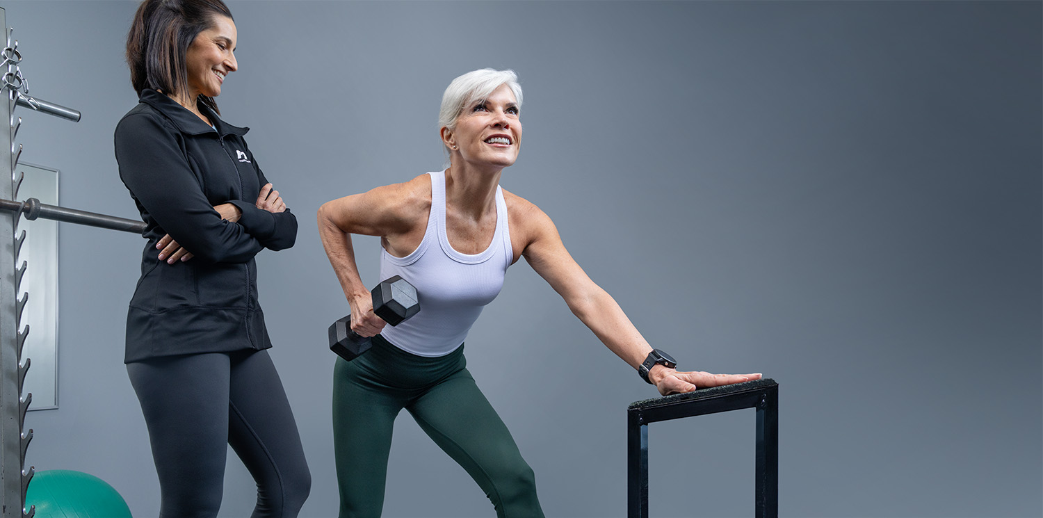 A Fitness Together female client performing a dumbbell lunge while her trainer looks on with confidence — private studio training in Raleigh Hills