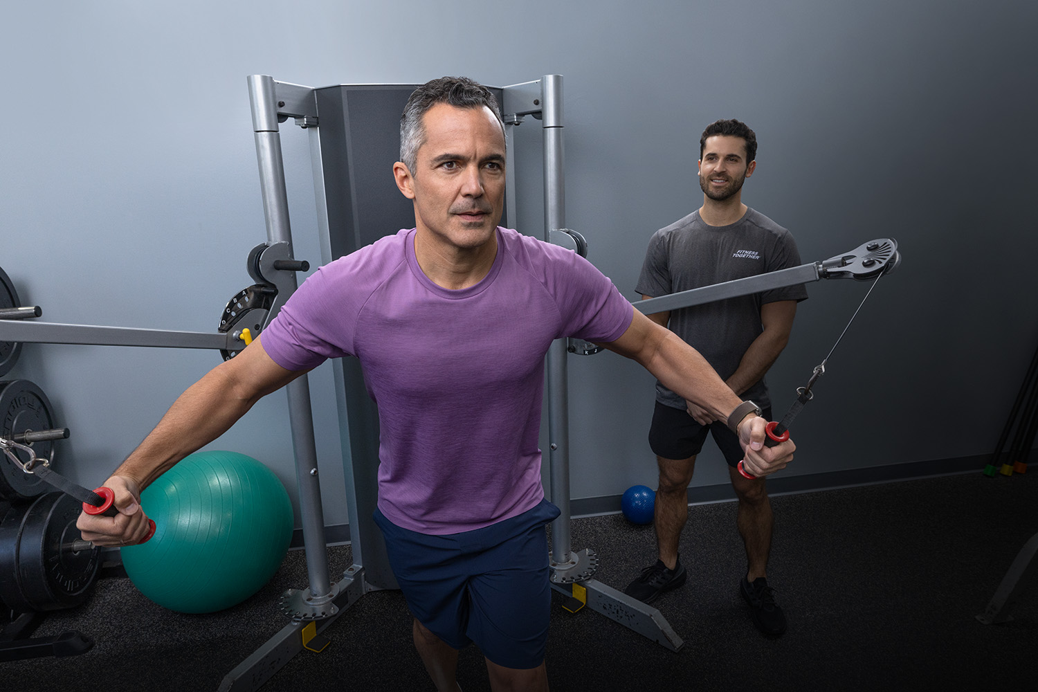 A Fitness Together client mid-workout on a rower with his trainer tracking progress on a tablet