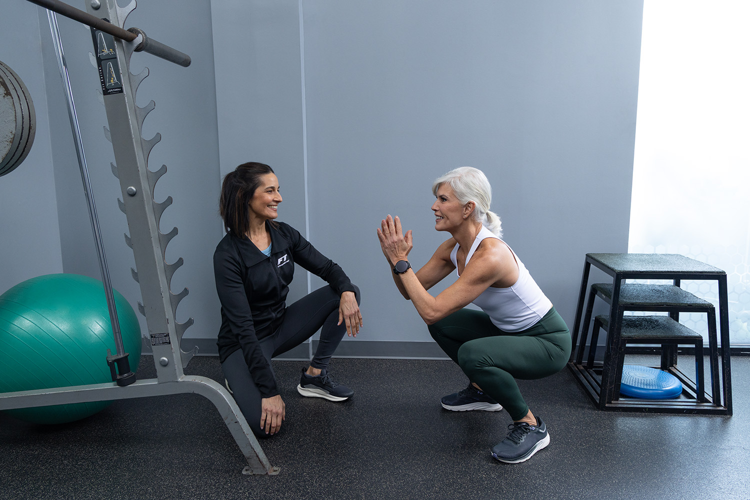 A Fitness Together female client and her trainer sharing a smile mid-squat — the 'We're In This Together' promise in action