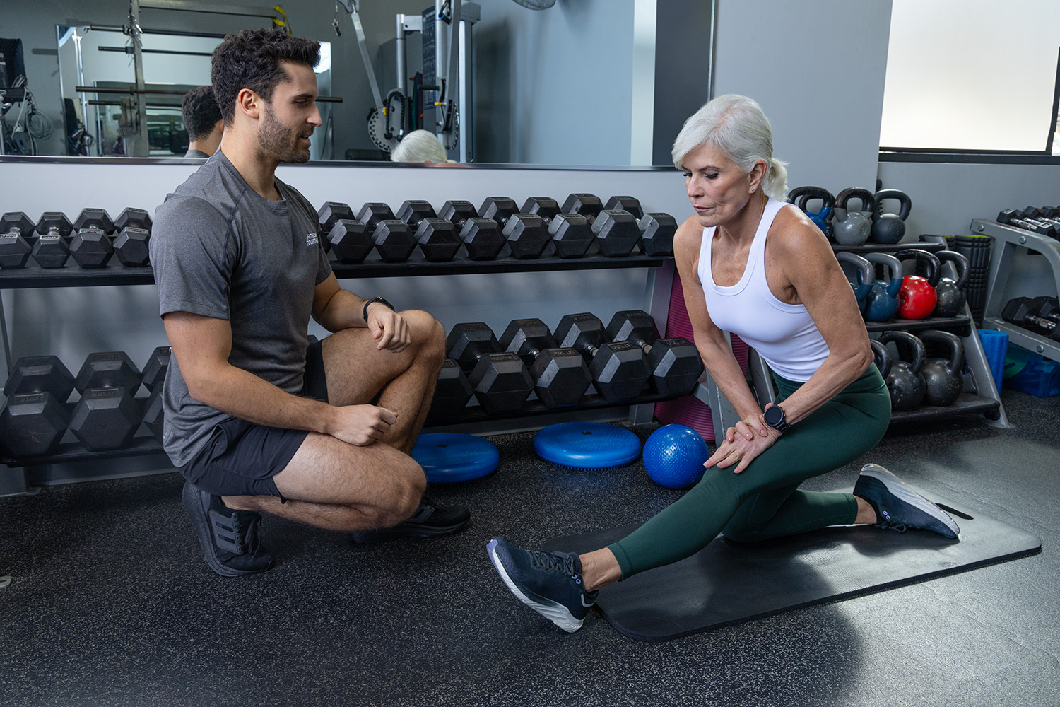 A Fitness Together female client performing a dumbbell row in a private training suite while her certified trainer guides her form